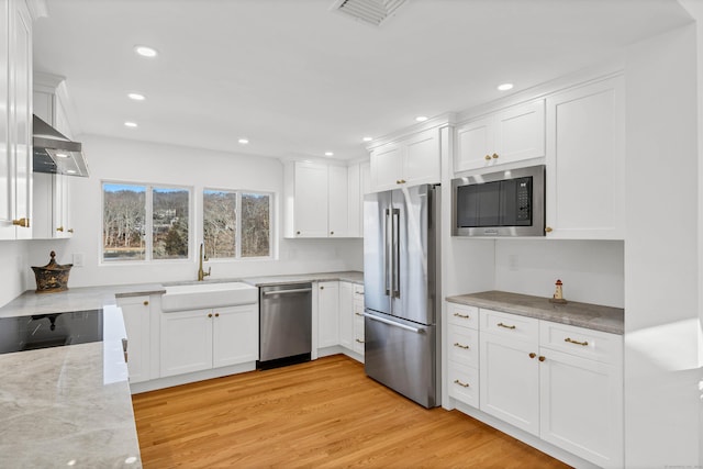 kitchen with a sink, extractor fan, white cabinetry, appliances with stainless steel finishes, and light stone countertops