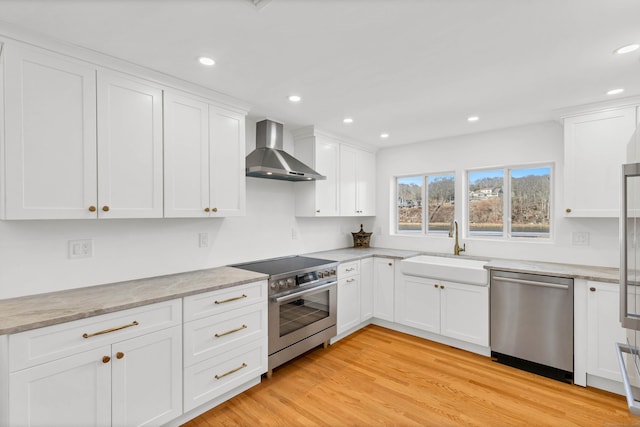 kitchen with stainless steel appliances, a sink, light wood-style floors, white cabinetry, and wall chimney range hood