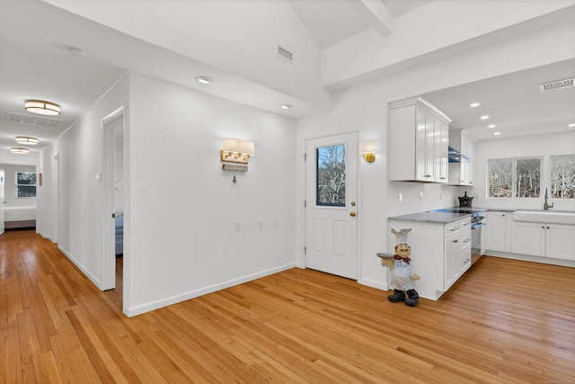 kitchen with high end stainless steel range, visible vents, white cabinets, and light wood-style floors