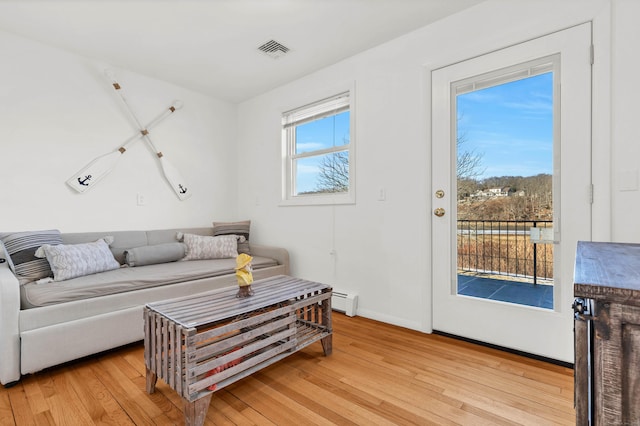 living area featuring light wood finished floors, baseboards, visible vents, and a baseboard heating unit