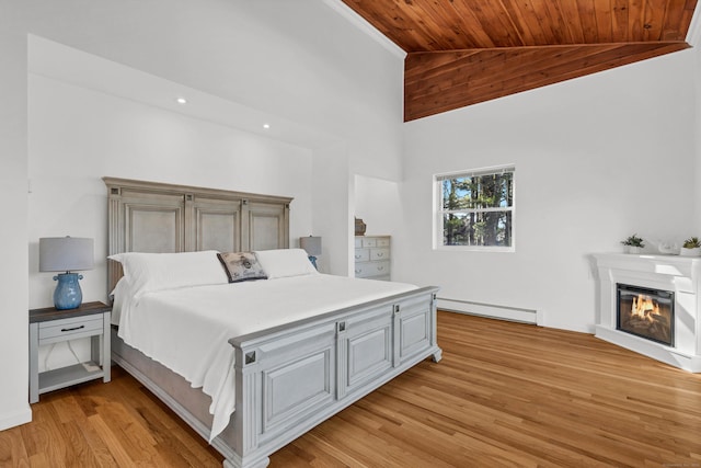 bedroom with a baseboard heating unit, light wood finished floors, a glass covered fireplace, wood ceiling, and high vaulted ceiling