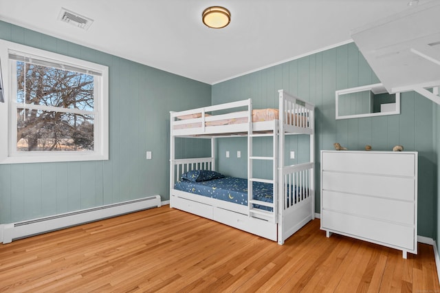 bedroom with a baseboard heating unit, wood finished floors, and visible vents