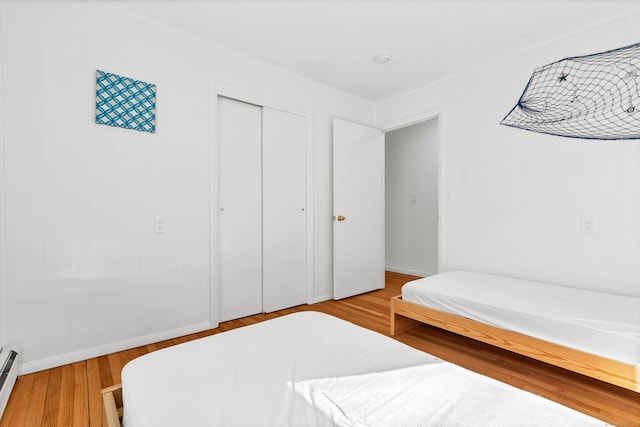 bedroom with a baseboard heating unit, baseboards, wood finished floors, and a closet