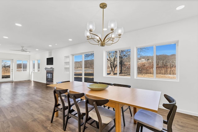dining room featuring wood finished floors, a stone fireplace, a wealth of natural light, a notable chandelier, and recessed lighting