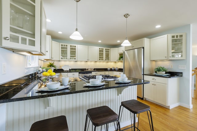 kitchen featuring stovetop, glass insert cabinets, stainless steel fridge, light wood-style flooring, and a peninsula