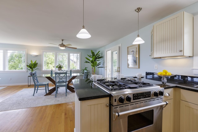kitchen with cream cabinets, light wood-style floors, pendant lighting, stainless steel range with gas stovetop, and a ceiling fan