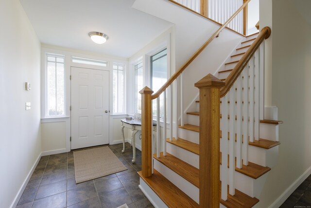 entrance foyer featuring dark tile patterned flooring, stairs, and baseboards