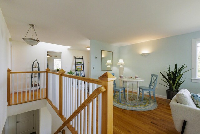 hallway featuring baseboards, wood finished floors, and an upstairs landing