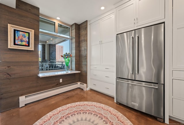 interior space with white cabinets, finished concrete flooring, a baseboard heating unit, and high end refrigerator