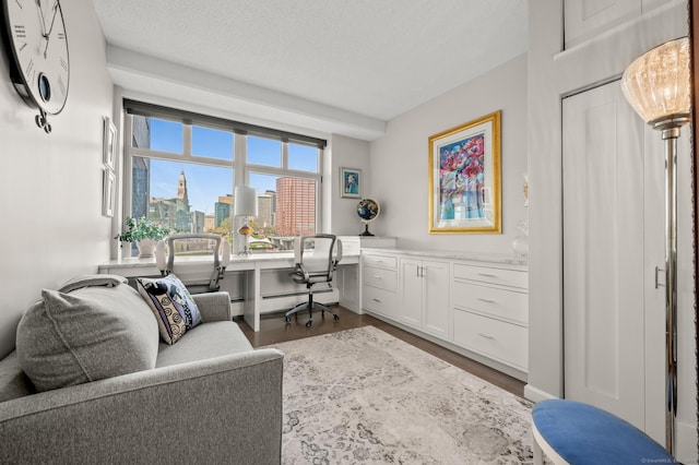 office area featuring built in desk, wood finished floors, a textured ceiling, a city view, and baseboard heating