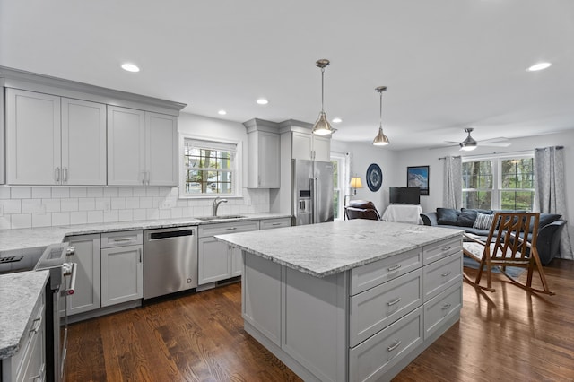 kitchen featuring appliances with stainless steel finishes, a sink, gray cabinetry, open floor plan, and healthy amount of natural light