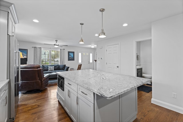 kitchen with black microwave, ceiling fan, dark wood finished floors, hanging light fixtures, and a kitchen island