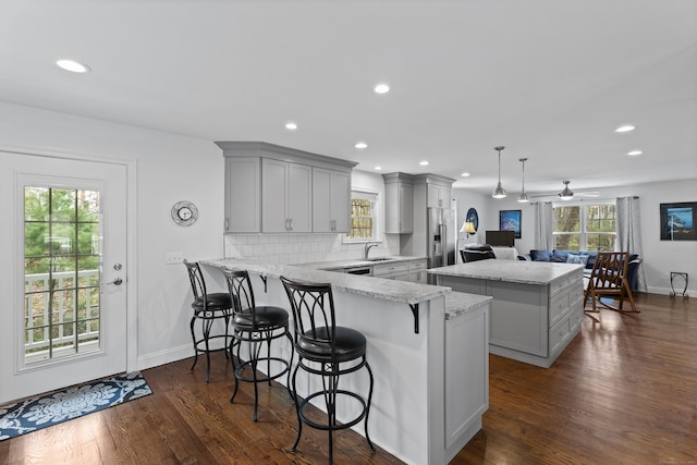 kitchen with gray cabinetry, a sink, a kitchen island, a peninsula, and plenty of natural light