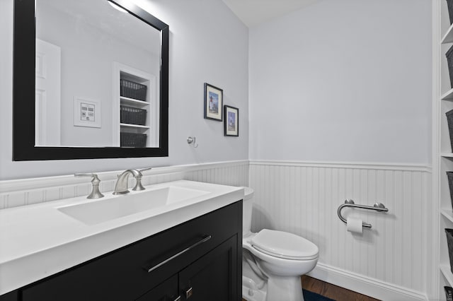 bathroom with a wainscoted wall, toilet, vanity, and wood finished floors