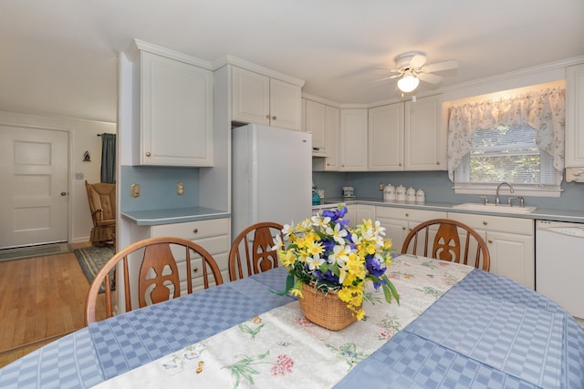 kitchen featuring white cabinets, a sink, white appliances, a ceiling fan, and wood finished floors
