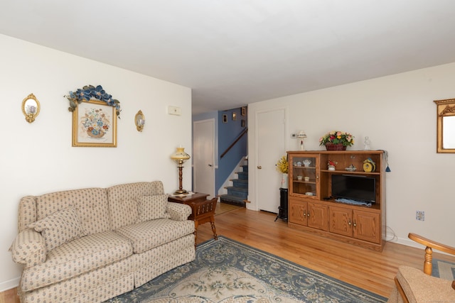 living room featuring baseboards, light wood-style flooring, and stairway
