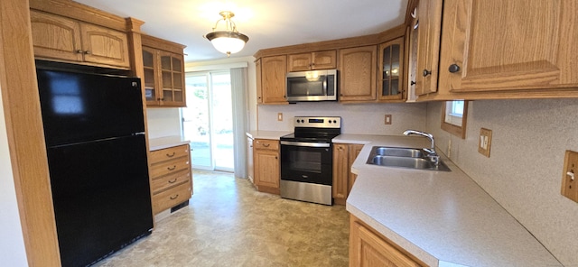 kitchen featuring glass insert cabinets, a sink, appliances with stainless steel finishes, light countertops, and light floors