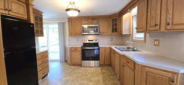 kitchen featuring glass insert cabinets, appliances with stainless steel finishes, light countertops, brown cabinets, and a sink