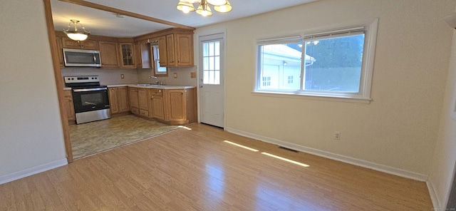 kitchen with a sink, a chandelier, stainless steel appliances, baseboards, and light wood finished floors