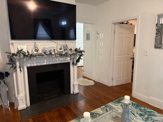 living room featuring a fireplace with flush hearth, hardwood / wood-style flooring, and baseboards