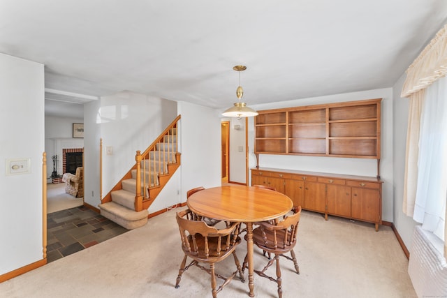 dining room featuring baseboards, a fireplace, stairway, and light colored carpet
