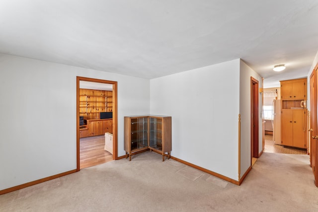 spare room featuring baseboards and light carpet