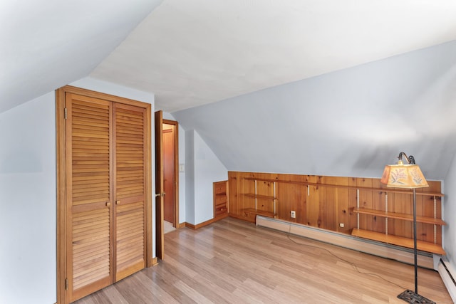 additional living space featuring baseboards, light wood finished floors, a baseboard heating unit, and vaulted ceiling