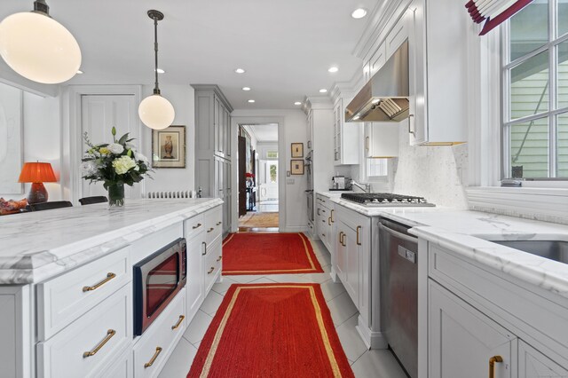 259 N Main St, Stonington, CT 06378 - kitchen with appliances with stainless steel finishes, exhaust hood, backsplash, light stone counters, and decorative light fixtures