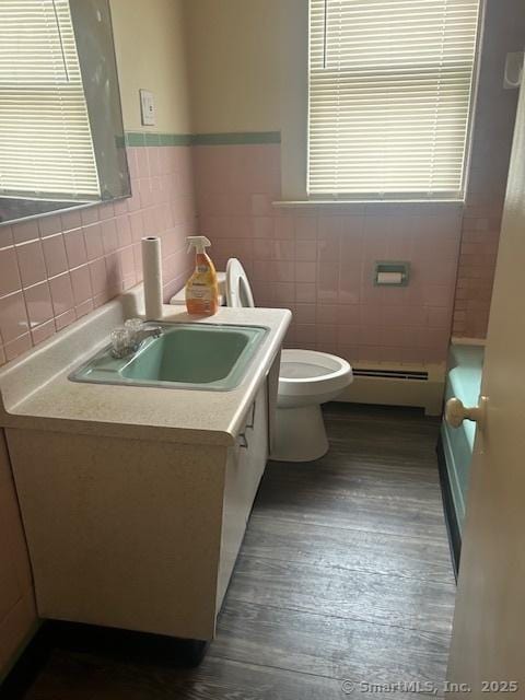 bathroom featuring a baseboard radiator, tile walls, vanity, wood finished floors, and toilet