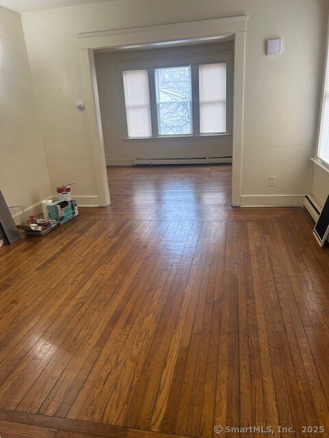 empty room with plenty of natural light, baseboards, and dark wood-style flooring