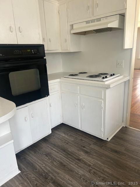 kitchen featuring oven, under cabinet range hood, white electric cooktop, dark wood finished floors, and light countertops