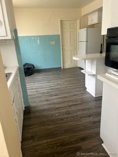 kitchen with black oven, white cabinetry, dark wood-style flooring, tile walls, and light countertops