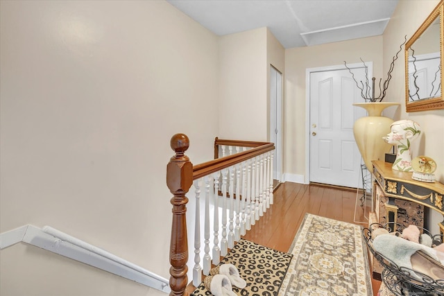 hall featuring wood-type flooring, baseboards, and an upstairs landing