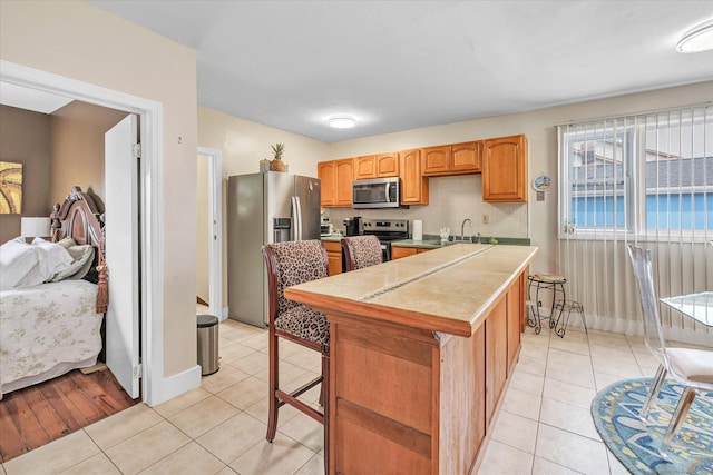 kitchen featuring a sink, tile counters, stainless steel appliances, light tile patterned floors, and a kitchen island
