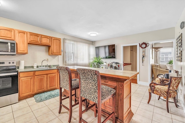 kitchen featuring light tile patterned flooring, light countertops, tasteful backsplash, a sink, and appliances with stainless steel finishes
