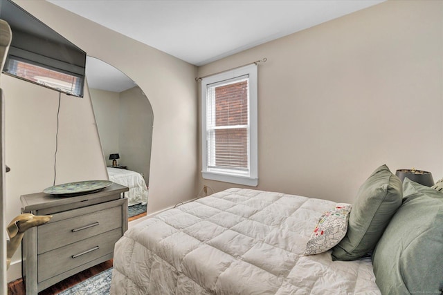 bedroom with arched walkways and wood finished floors