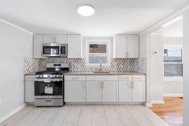 kitchen featuring decorative backsplash, stainless steel appliances, a sink, baseboards, and crown molding