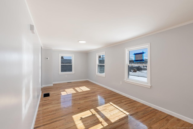 empty room with crown molding, light wood-type flooring, visible vents, and baseboards