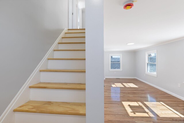 stairway with wood finished floors, ornamental molding, and baseboards