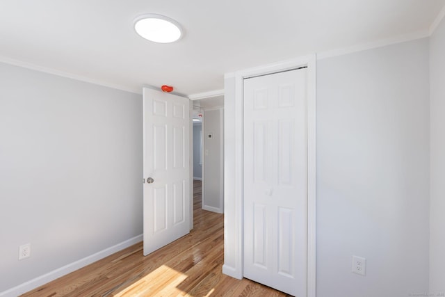 unfurnished bedroom featuring baseboards, crown molding, a closet, and light wood-style flooring