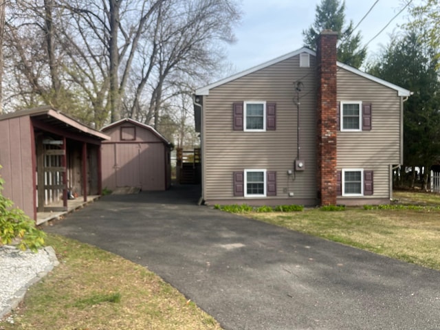 view of side of property featuring an outdoor structure, a chimney, a storage shed, a lawn, and aphalt driveway