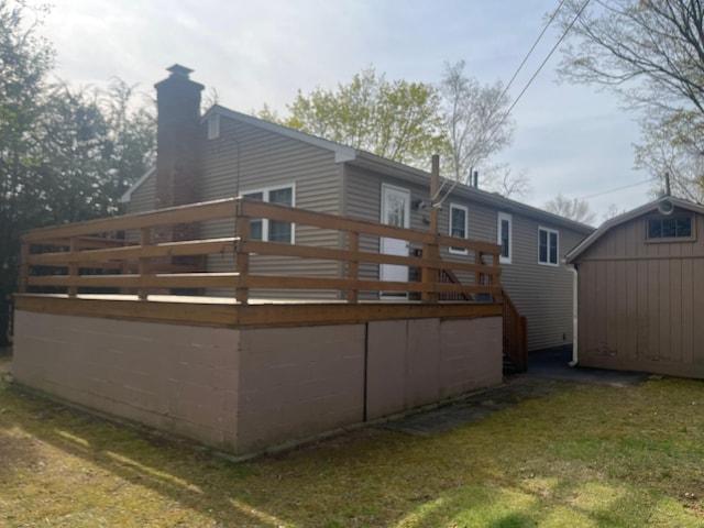 rear view of house featuring a chimney, an outdoor structure, a storage shed, a wooden deck, and a lawn