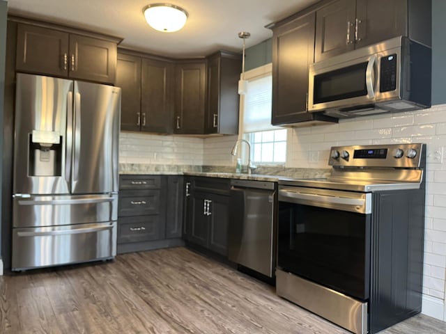 kitchen featuring light stone countertops, wood finished floors, hanging light fixtures, decorative backsplash, and stainless steel appliances