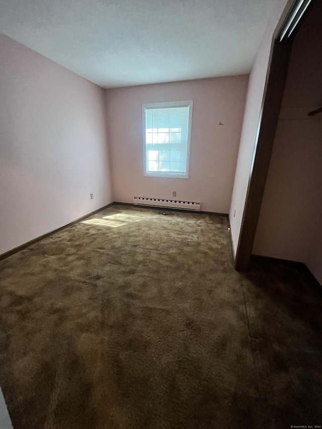 unfurnished bedroom with a baseboard heating unit, a closet, dark colored carpet, and baseboards