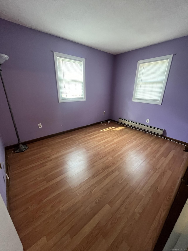 empty room with wood finished floors and a baseboard heating unit