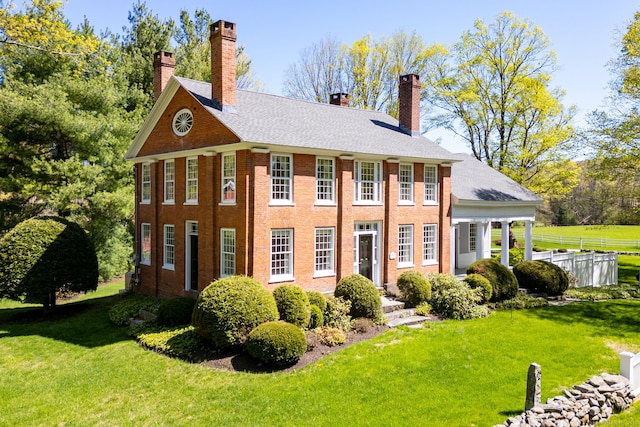 view of front of property with fence, a chimney, a front lawn, and brick siding