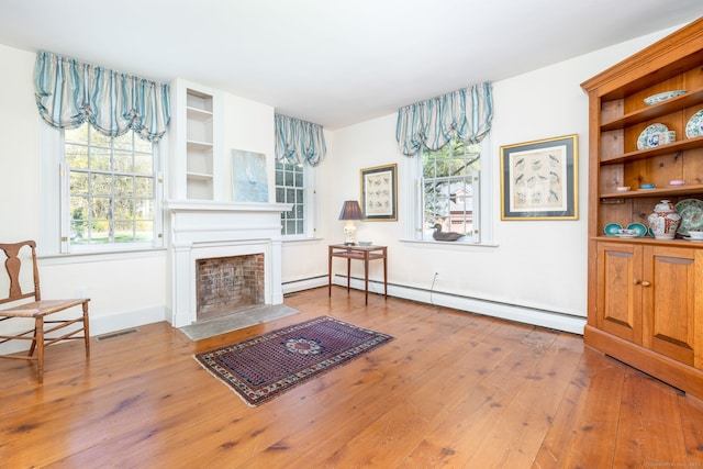 living area with visible vents, baseboards, a fireplace with flush hearth, wood finished floors, and a baseboard heating unit