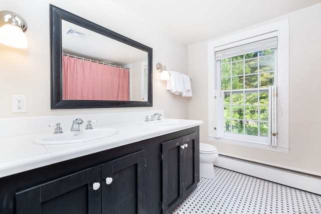 full bath featuring a sink, baseboard heating, toilet, and double vanity
