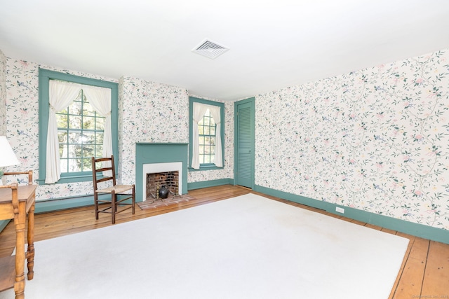 living area with a fireplace, baseboards, wallpapered walls, wood finished floors, and visible vents