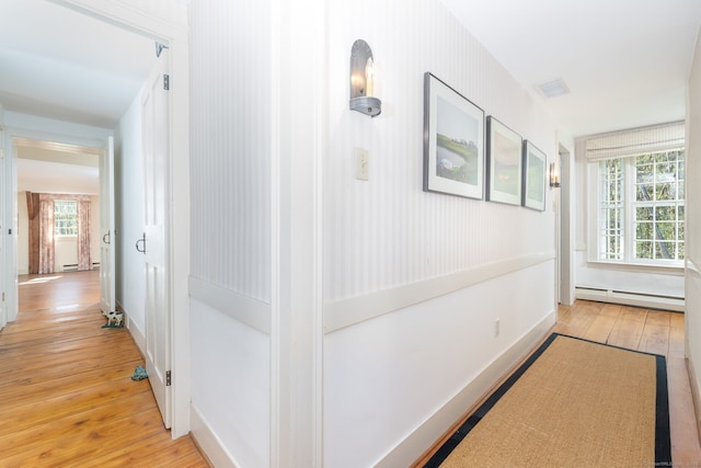 corridor featuring baseboards, a baseboard radiator, light wood finished floors, and visible vents
